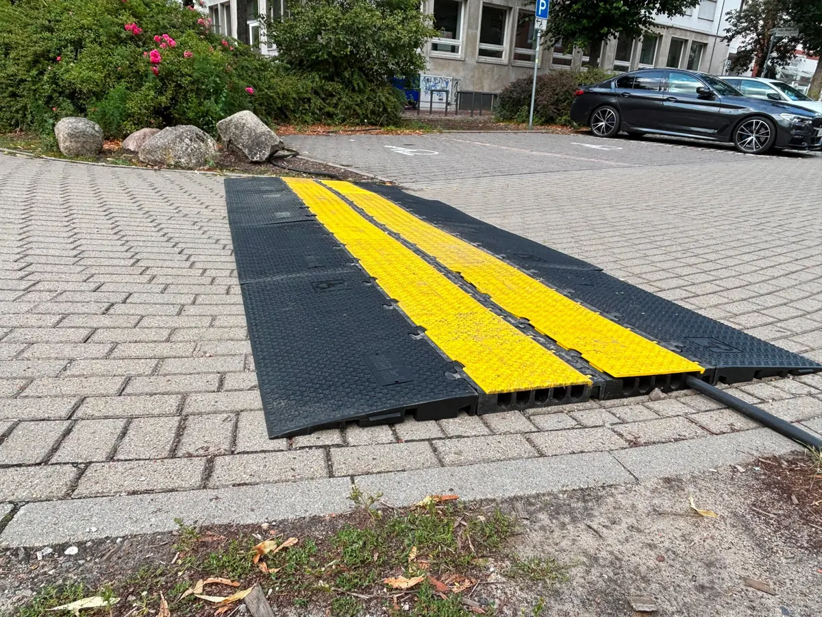 Gelbe und schwarze Kabelbrücken schützen verlegte Kabel auf einer gepflasterten Zufahrt