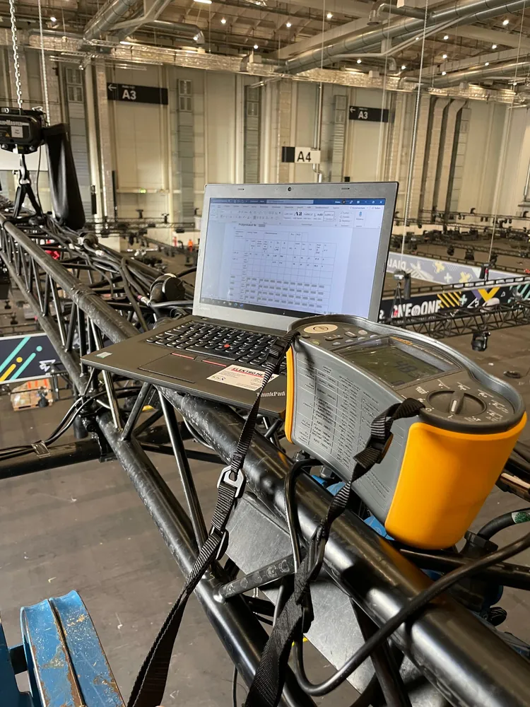 Elektrische Prüfung einer Veranstaltungsinstallation in einer Messehalle mit Installationstester und Laptop für das Prüfprotokoll